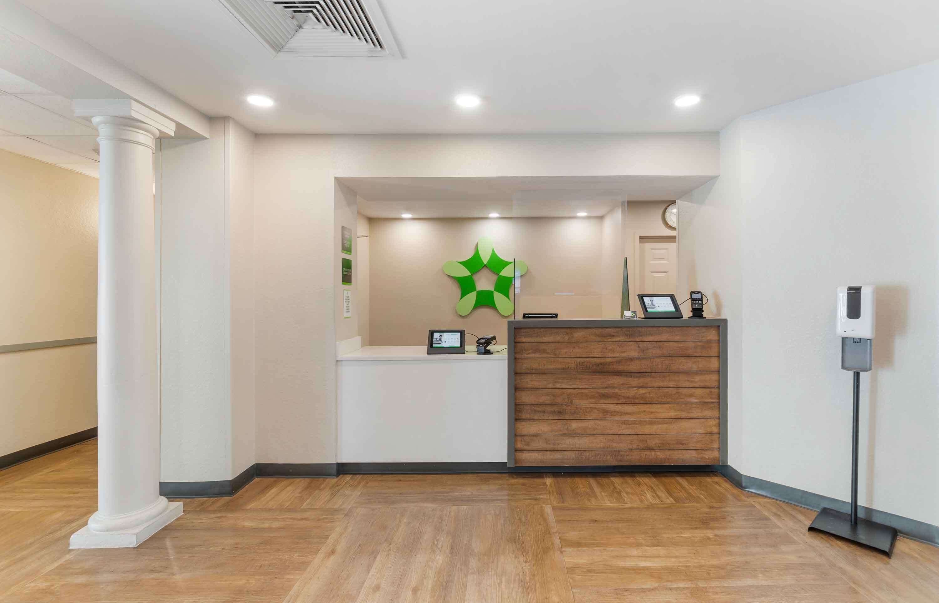 A reception area with a wooden reception desk, a green logo on the wall, a clock, and a standing air purifier.