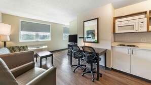 A modern hotel room with a kitchenette, a sofa, a dining table, and two office chairs.