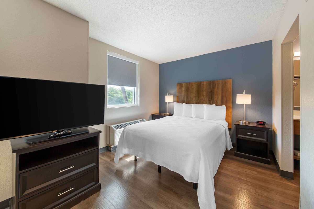 Una habitación de hotel con cama, televisión, calefacción y ventana.