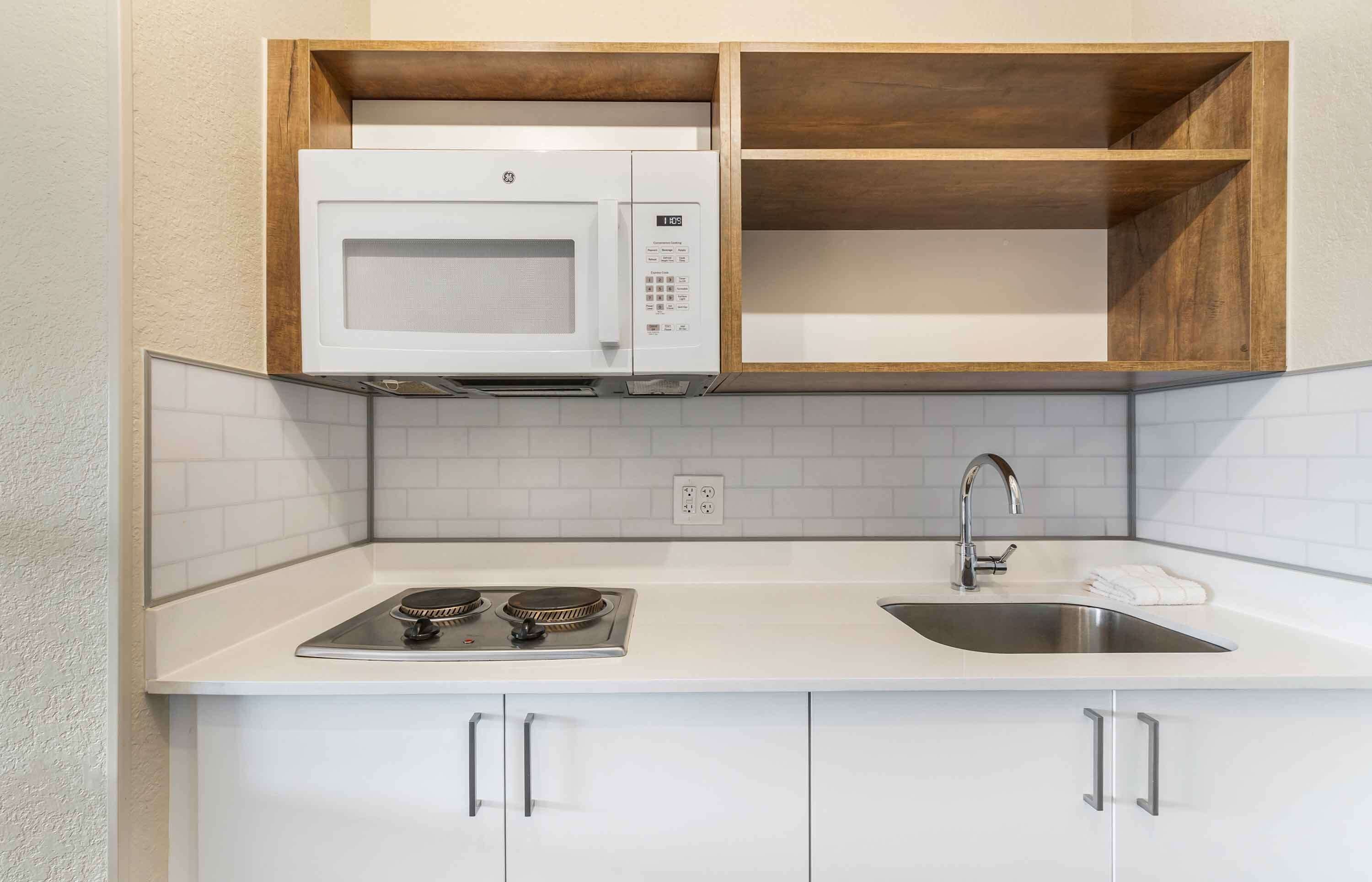 Cocina pequeña con microondas, estufa y lavamanos.