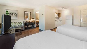 A hotel room with two beds, a desk with a chair, a television, a sofa, and a kitchenette.