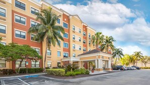 A multi-story hotel with a central courtyard, palm trees, and a parking area.