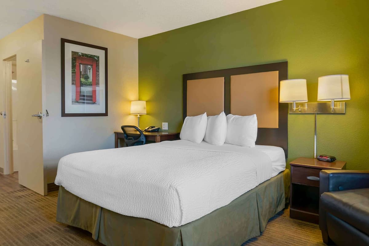 Una habitació d'hotel amb un llit gran, dues taules de nit amb làmpades, un escriptori amb una cadira i un quadre al mur.