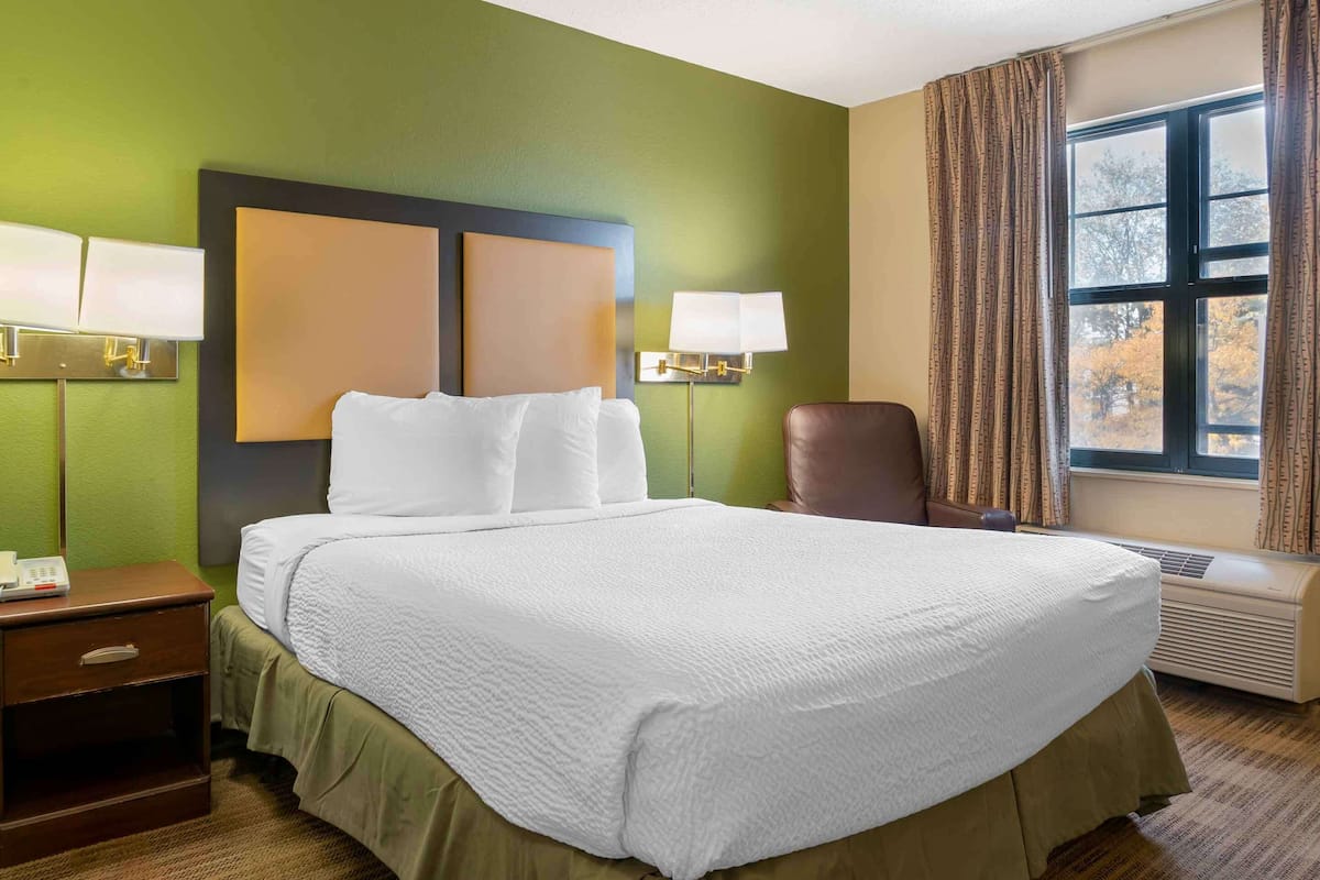 Habitació d'hotel amb un llit gran, dues làmpades de nit, una cadira i una finestra amb cortines.