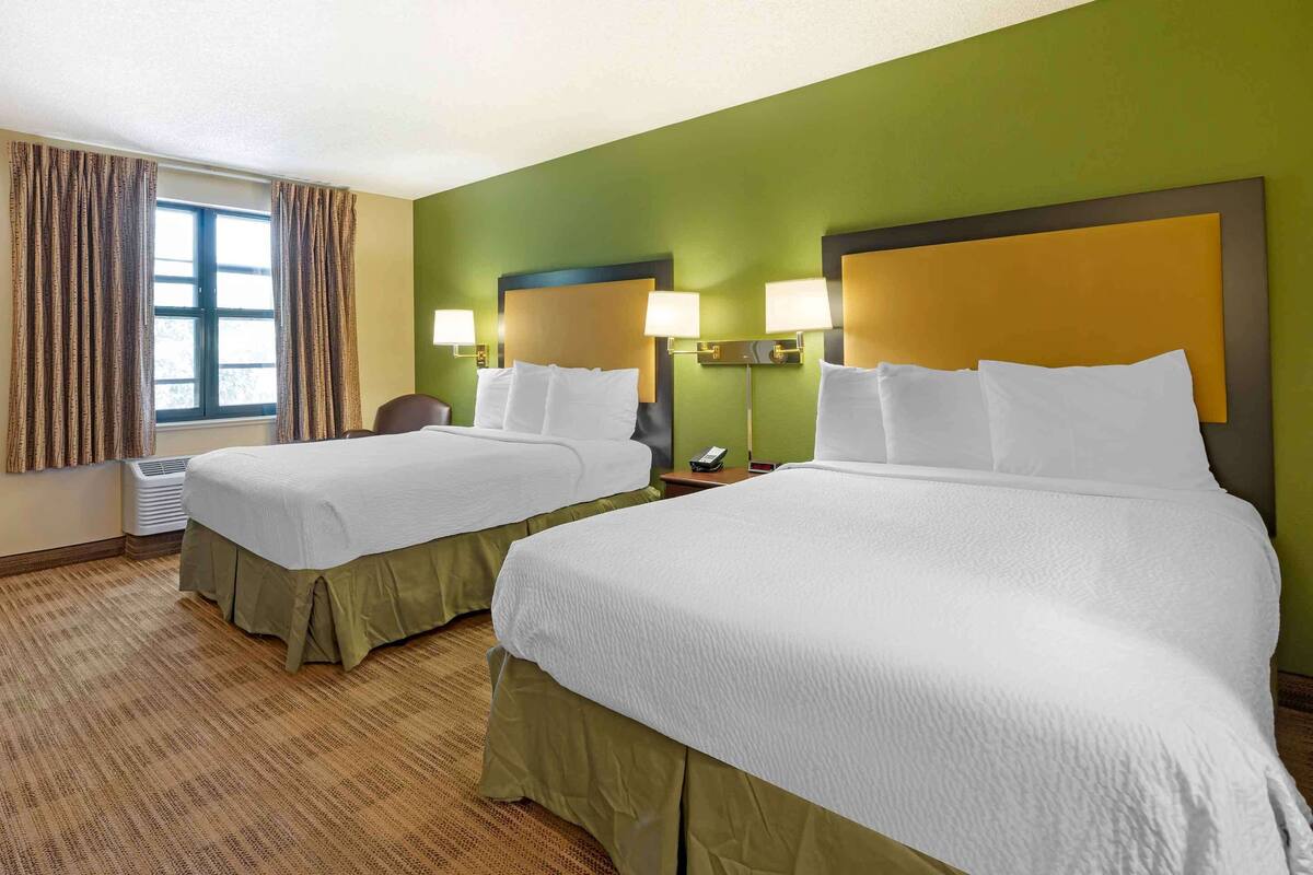 Habitación de hotel con dos camas, paredes verdes y una ventana con cortinas.