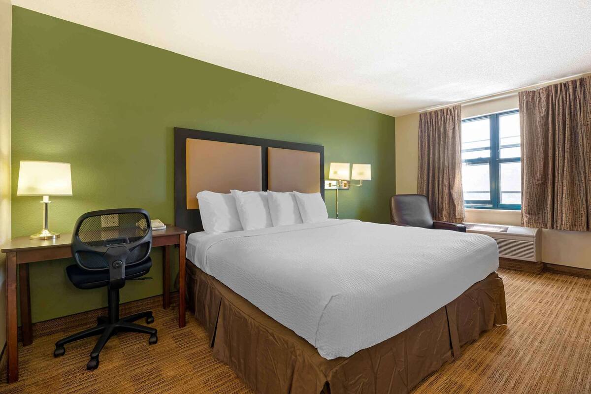 Una habitación de hotel con una cama grande, un escritorio con silla, una lámpara y una ventana con cortinas.