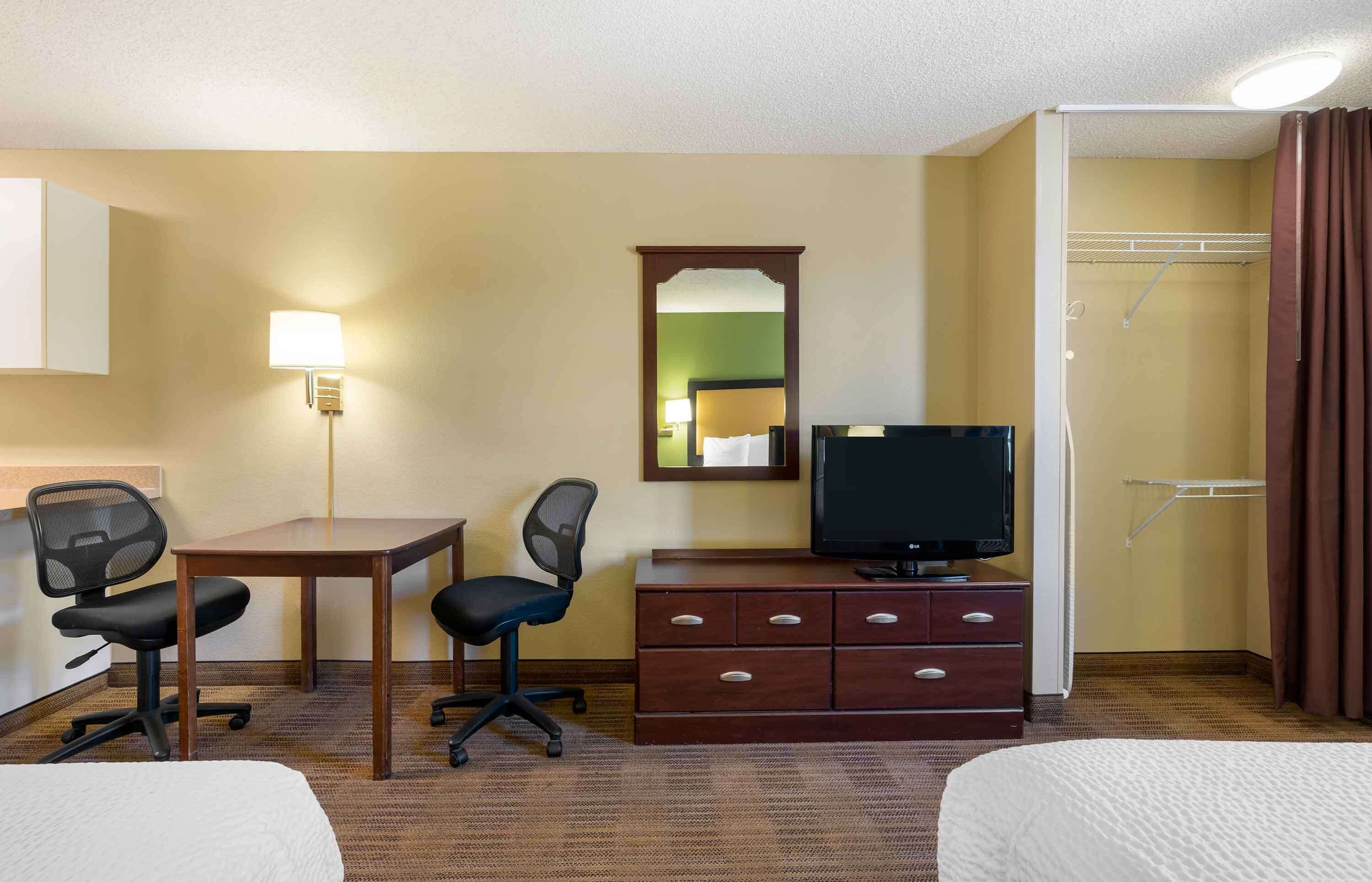 Ein Hotelzimmer mit einem Bett, einem Schreibtisch mit zwei Stühlen, einem Fernseher, einem Schminktisch und einer Dusche.