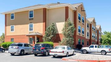 A multi-story hotel with a beige and brown facade, parking lot with several cars, and a small entrance with a canopy.