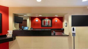 A hotel reception area with a black reception desk, a flat-screen TV mounted on the wall, a digital kiosk, and a framed picture of a door. - Extended Stay America Suites Reno South Meadows (Reno)