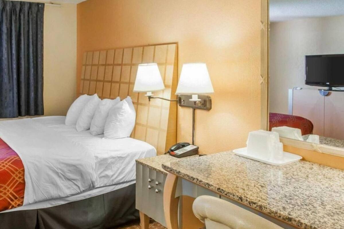 Une chambre d’hôtel avec un lit, deux lampes de chevet, un bureau avec un téléphone, une tasse et un téléviseur.