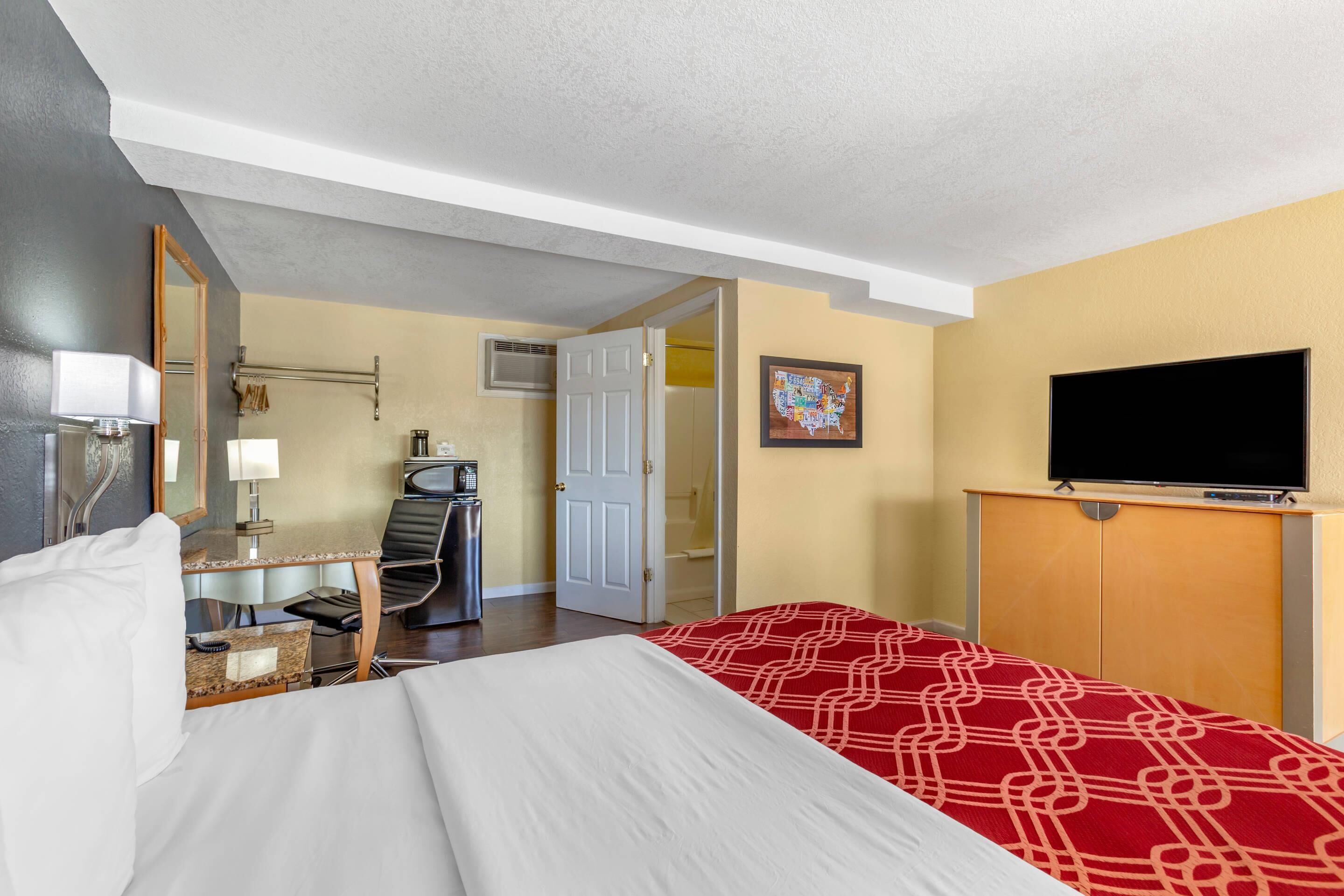A hotel room with a bed, desk, chair, TV, and a door leading to a bathroom.