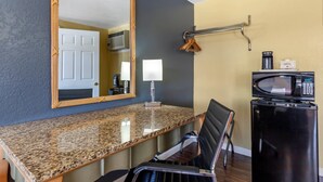 A compact hotel room with a granite countertop, a black refrigerator, a microwave, a hanging coat rack, and a door leading to a bathroom. - Econo Lodge Clovis (Clovis)