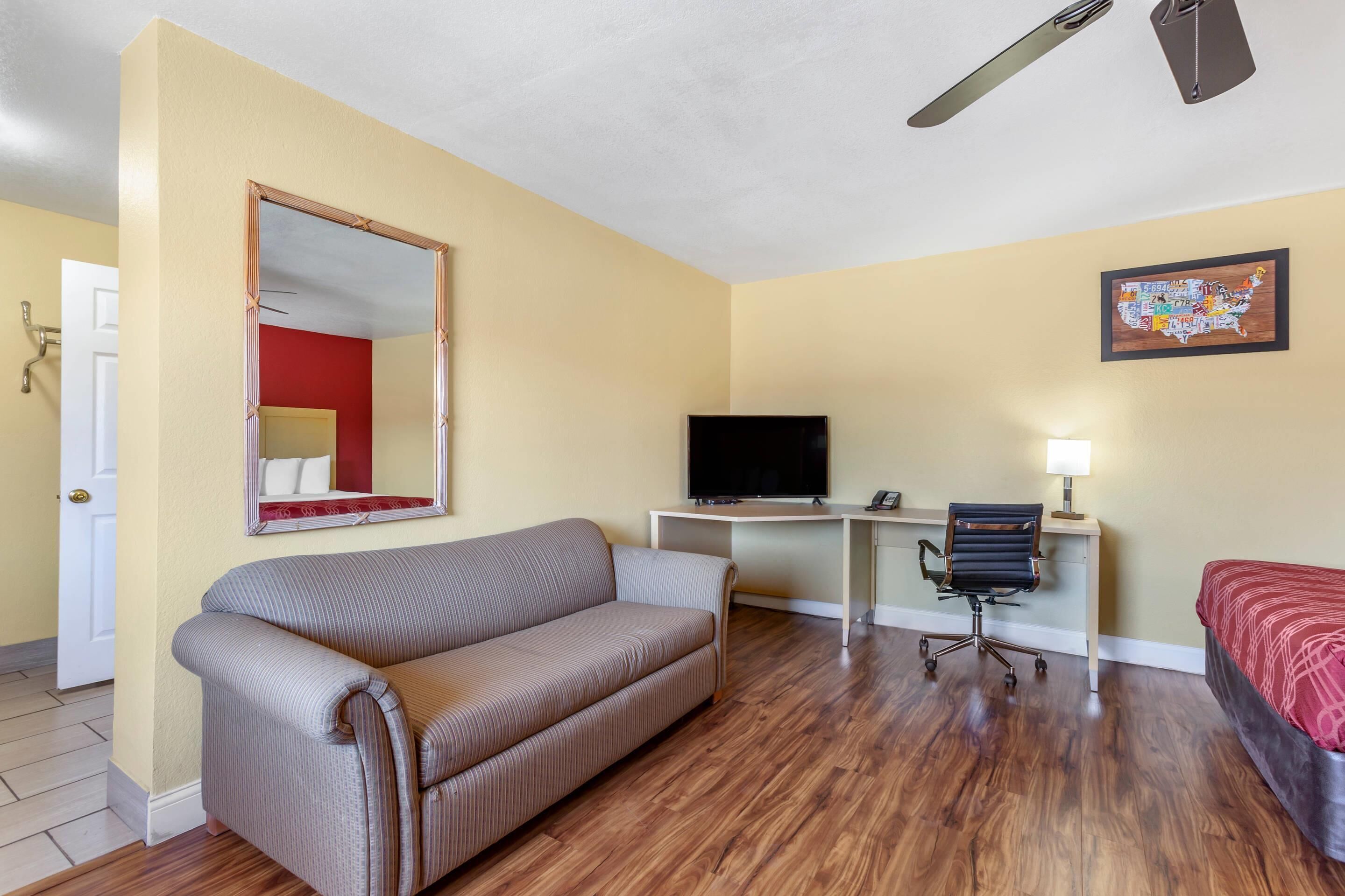 Une pièce comprenant un canapé, un bureau avec un ordinateur et une télévision, une chaise et un lit.