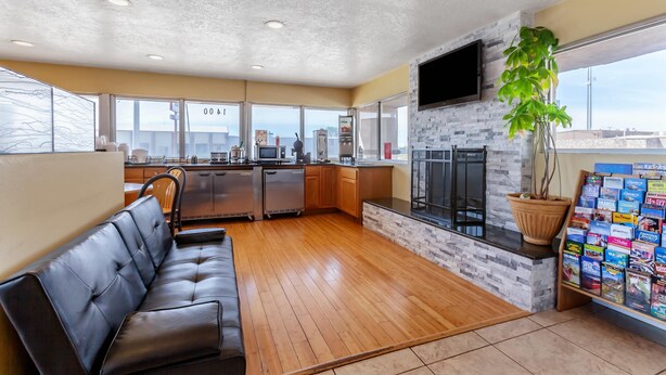 A modern kitchen with a stone backsplash, wooden cabinets, and a built-in oven. There is a black leather sofa and a large window offering a view of the city. - Econo Lodge Clovis (Clovis)