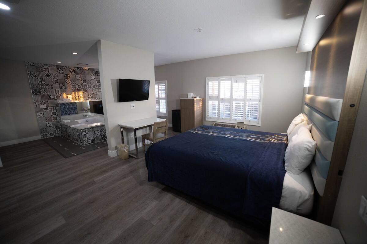 A modern bedroom with a large bed, a desk, and a built-in shower area.