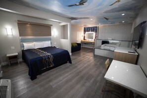 A modern hotel room with a bed, desk, and kitchenette. - Mid City Inn and Suites (Pico Rivera)
