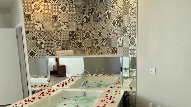 A bathroom with a large bathtub, patterned tiles, and a mirror. - Mid City Inn and Suites (Pico Rivera)