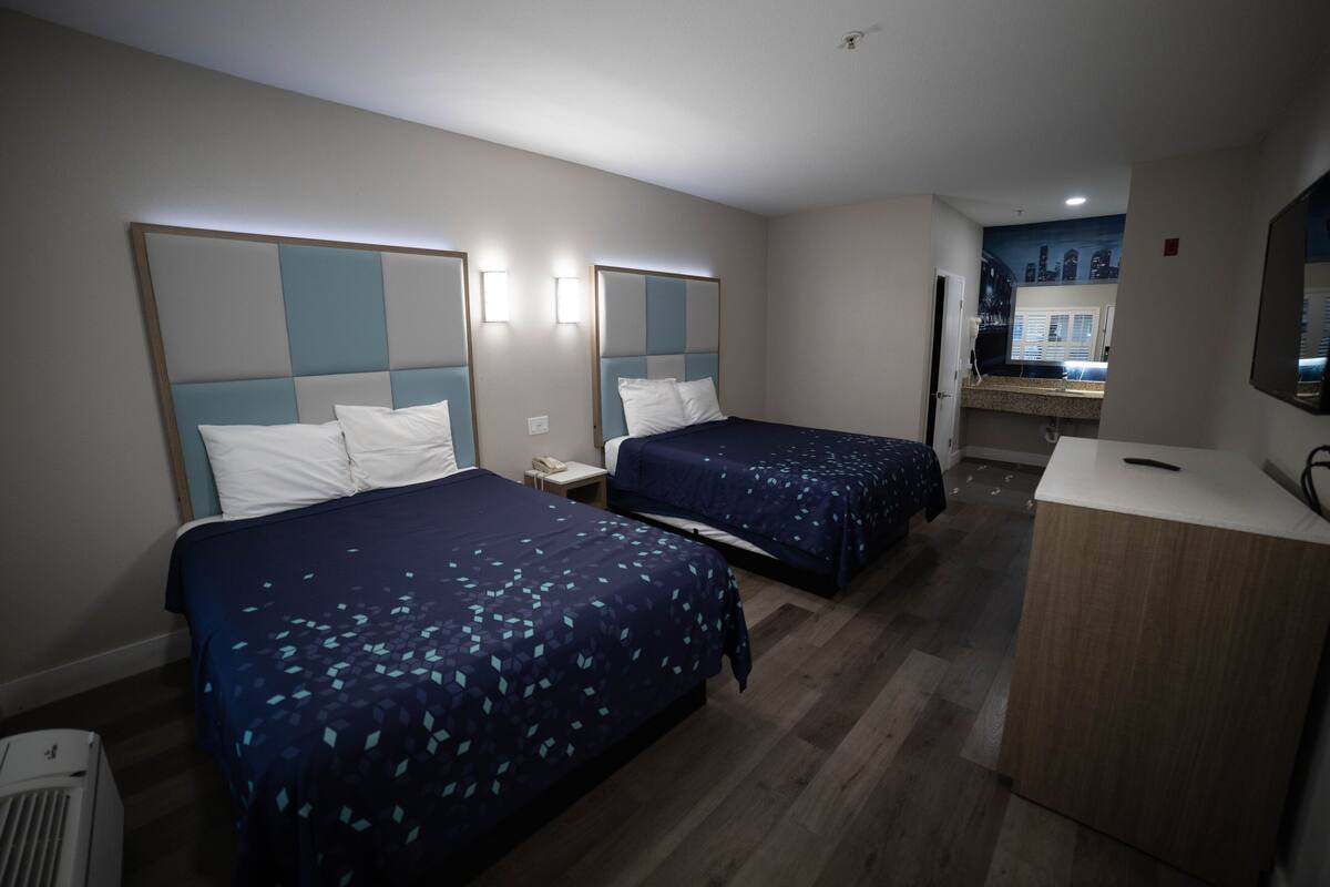 A hotel room with two beds, a desk, and a mirror.