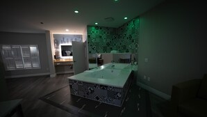 A modern bathroom with a large bathtub, a vanity with a mirror, and a patterned wall. - Mid City Inn and Suites (Pico Rivera)