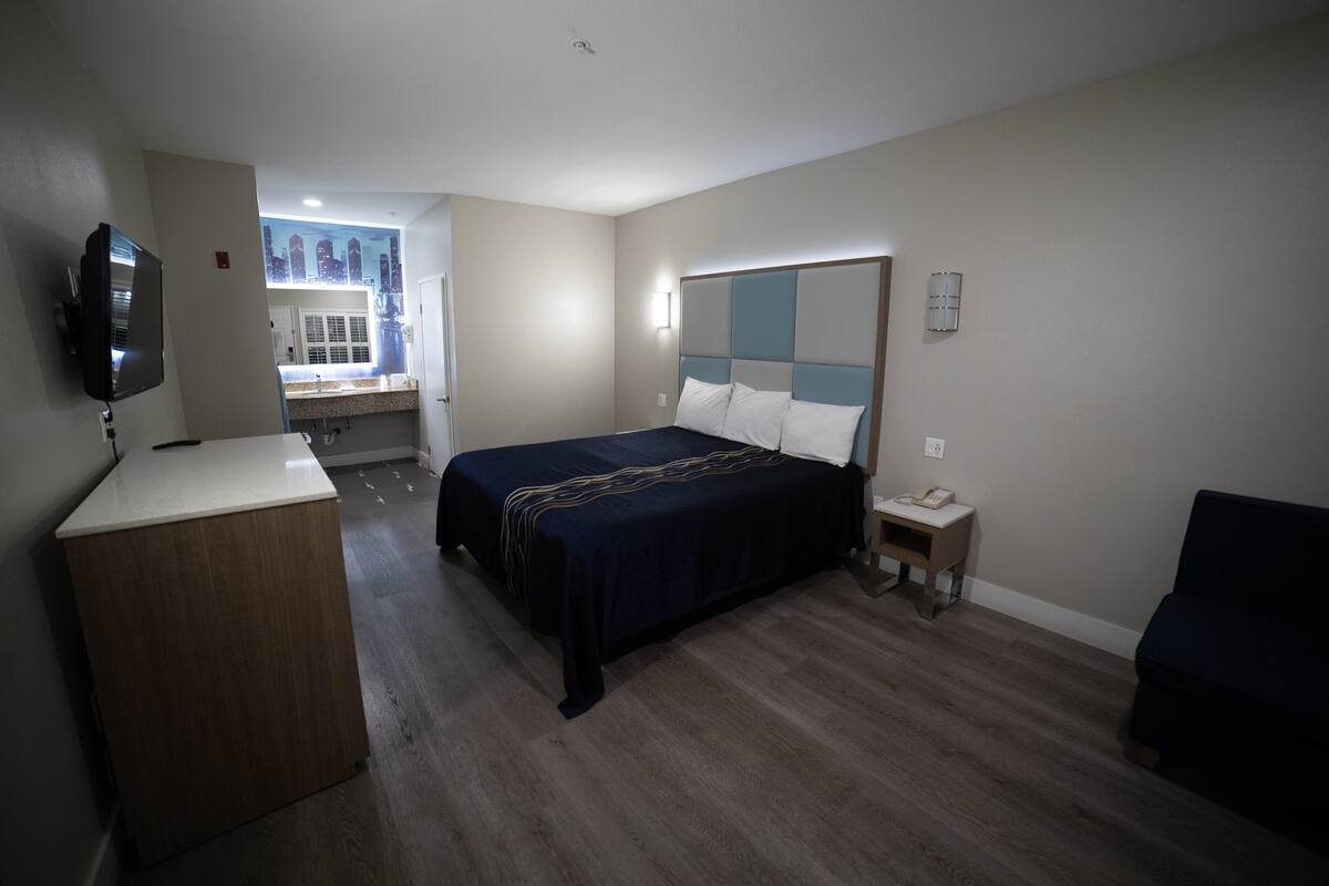 A hotel room with a bed, a desk, a TV, and a view of the cityscape through the window.