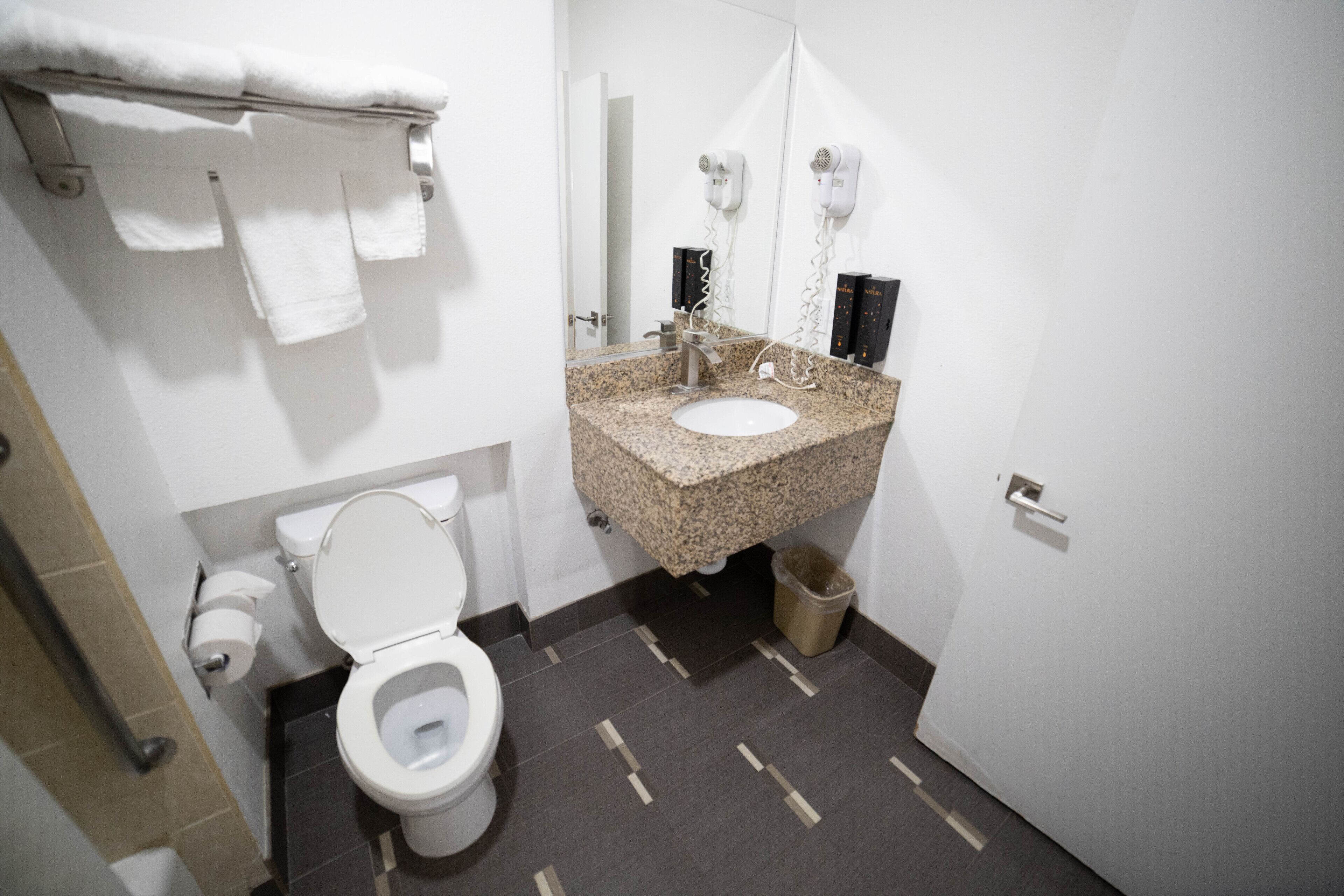 A bathroom with a white toilet, granite sink, and a mirror with a hairdryer.