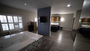 A modern hotel room with a large bathtub, a television mounted on the wall, and a bed with a headboard. - Mid City Inn and Suites (Pico Rivera)