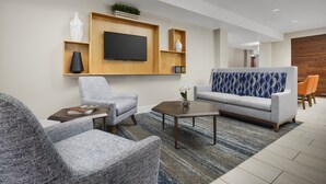 A modern living room with a grey sofa, two armchairs, a coffee table, and a flat-screen TV mounted on a wooden shelf. - Holiday Inn Express Rochester NE- Irondequoit by IHG (Rochester)