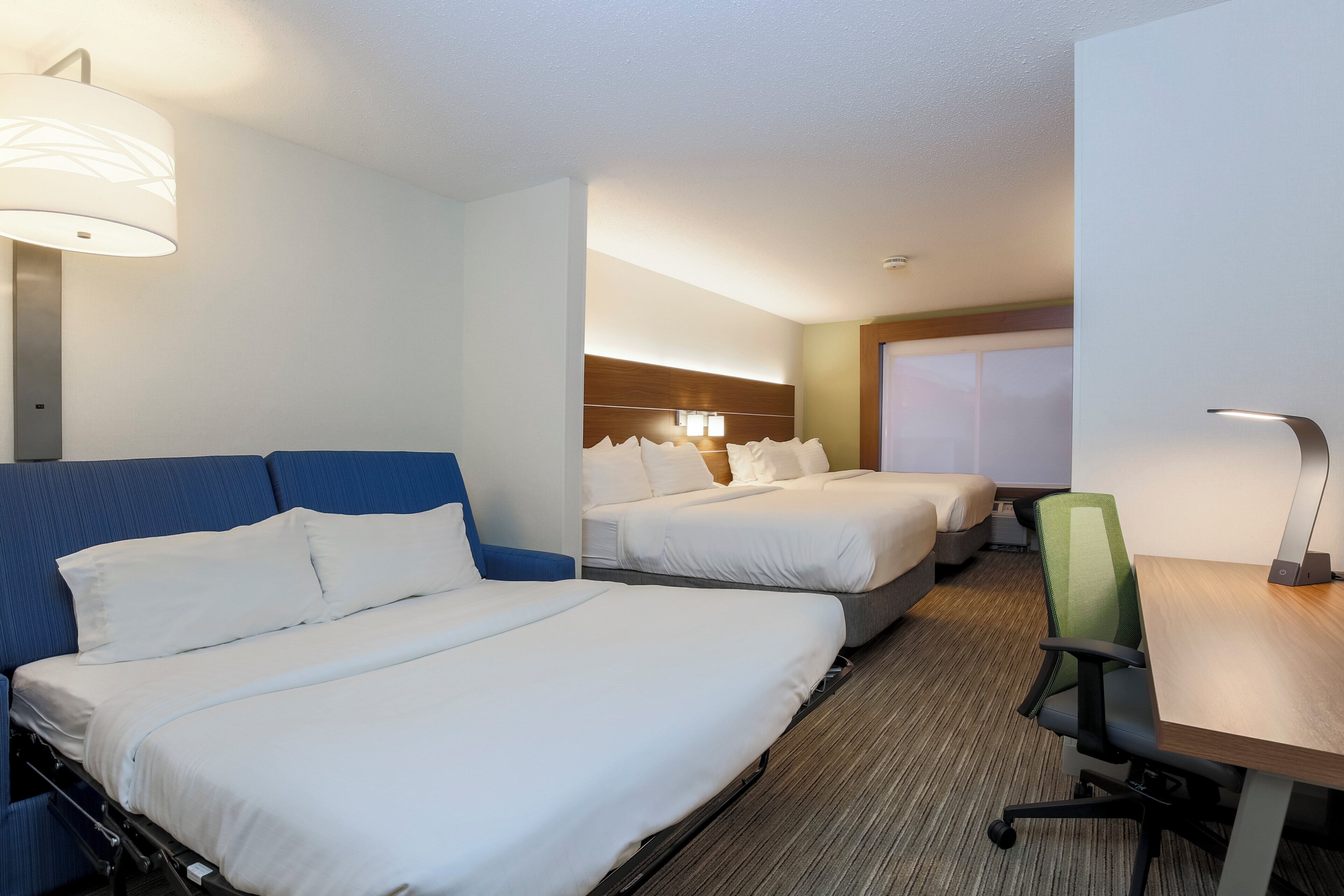 A hotel room with two beds, a desk, and a chair.