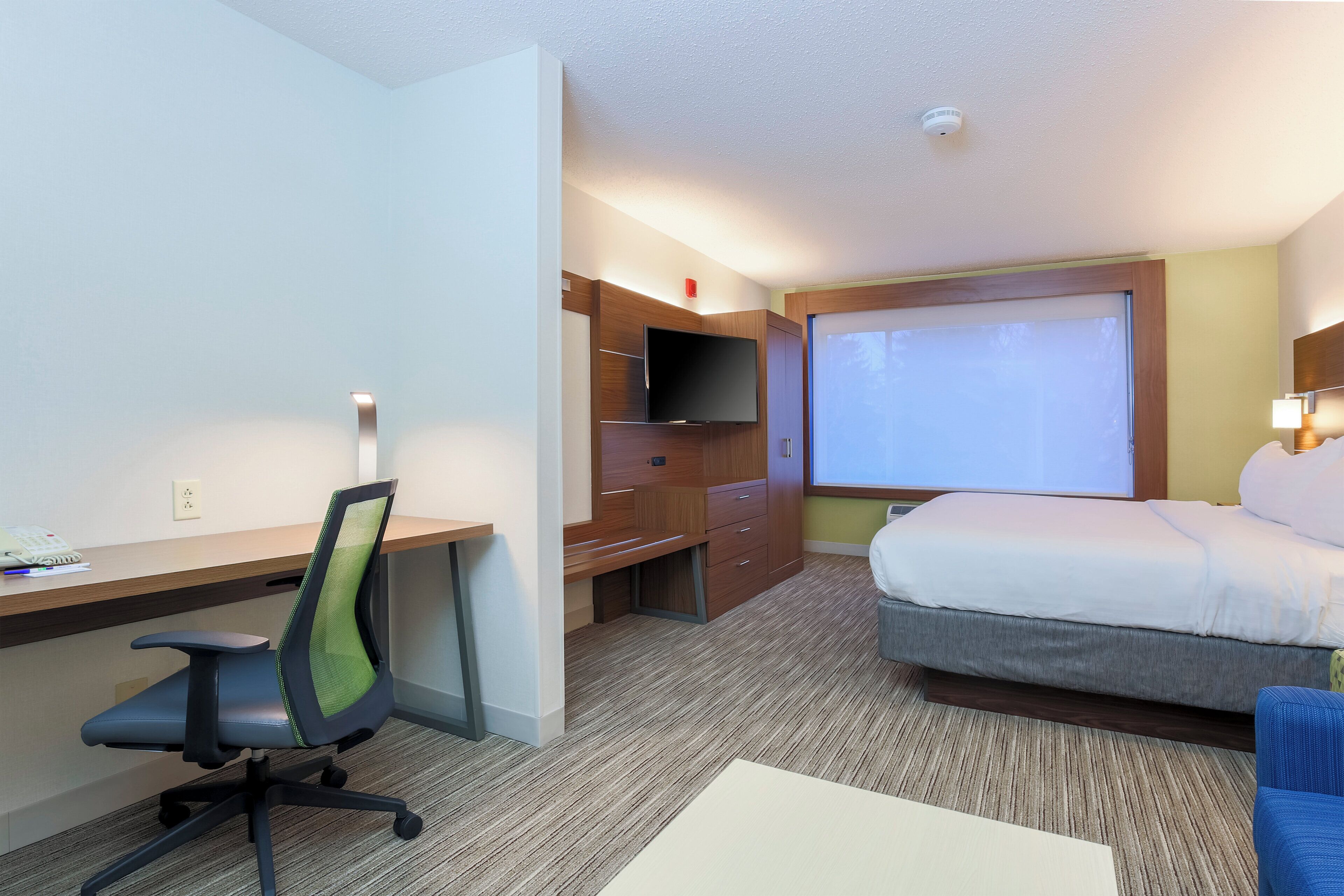 Ein Hotelzimmer mit einem Bett, einem Schreibtisch, einem Sessel, einem Fernseher und einem Fenster.