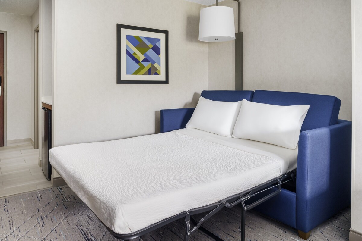 Una habitación moderna con una cama, un cuadro abstracto enmarco y una lámpara de pie.
