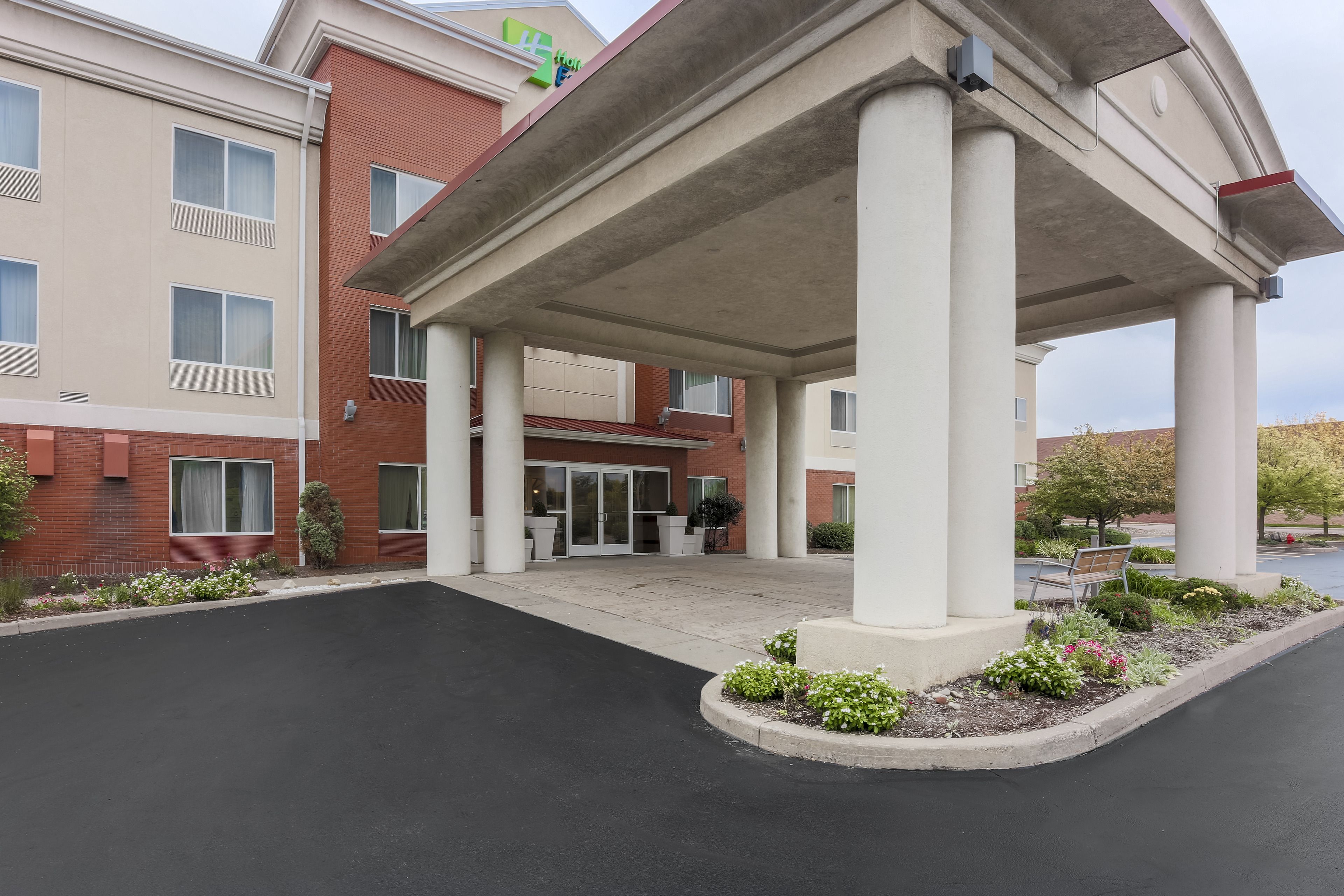 A hotel entrance with a covered walkway, a brick facade, and a landscaped area with plants and a bench.