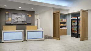 A Holiday Inn Express reception area with a modern design, including a reception desk, a wall-mounted sign, and a beverage refrigerator. - Holiday Inn Express Rochester NE- Irondequoit by IHG (Rochester)