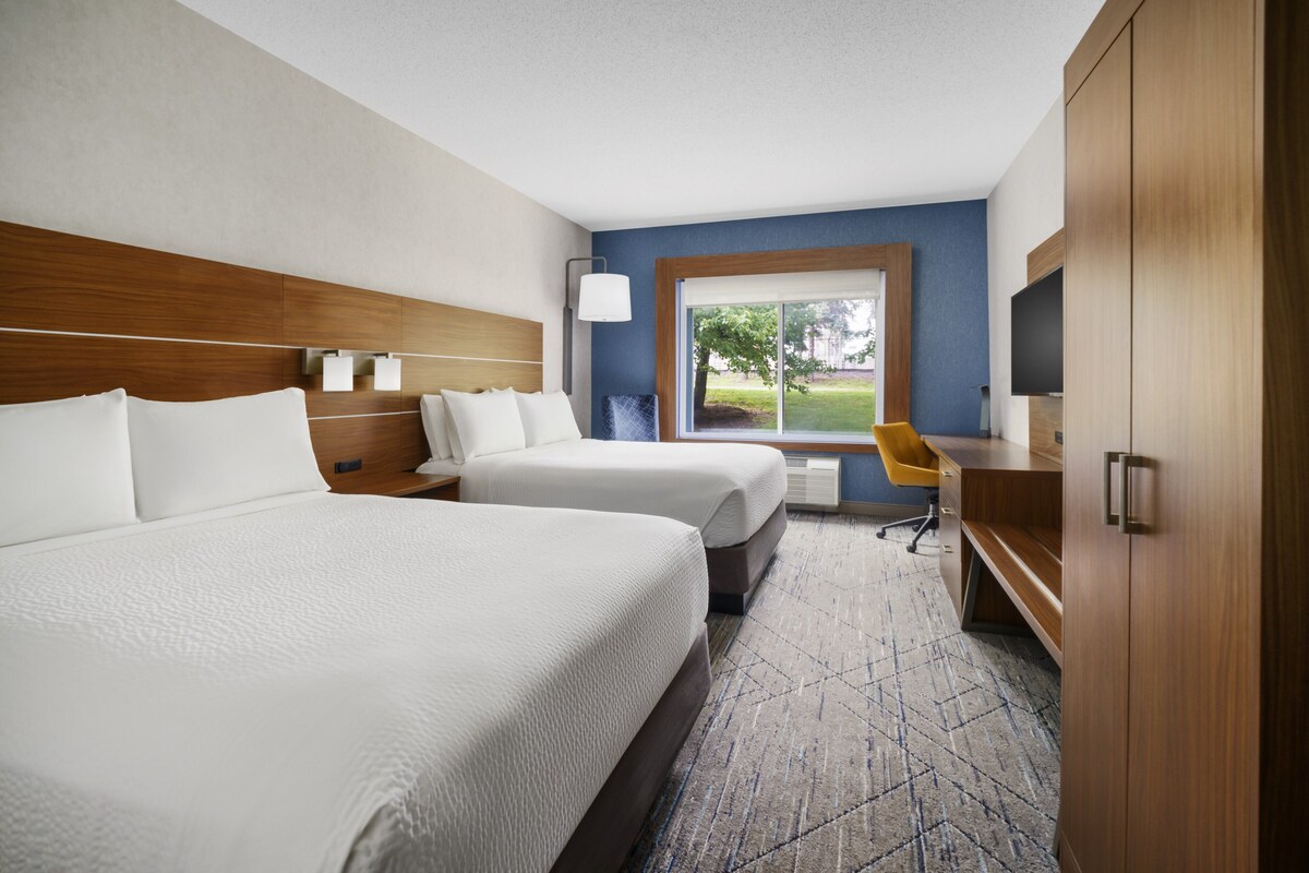 Habitación de hotel con dos camas, un escritorio, una silla, un televisor y una ventana con vistas al exterior.