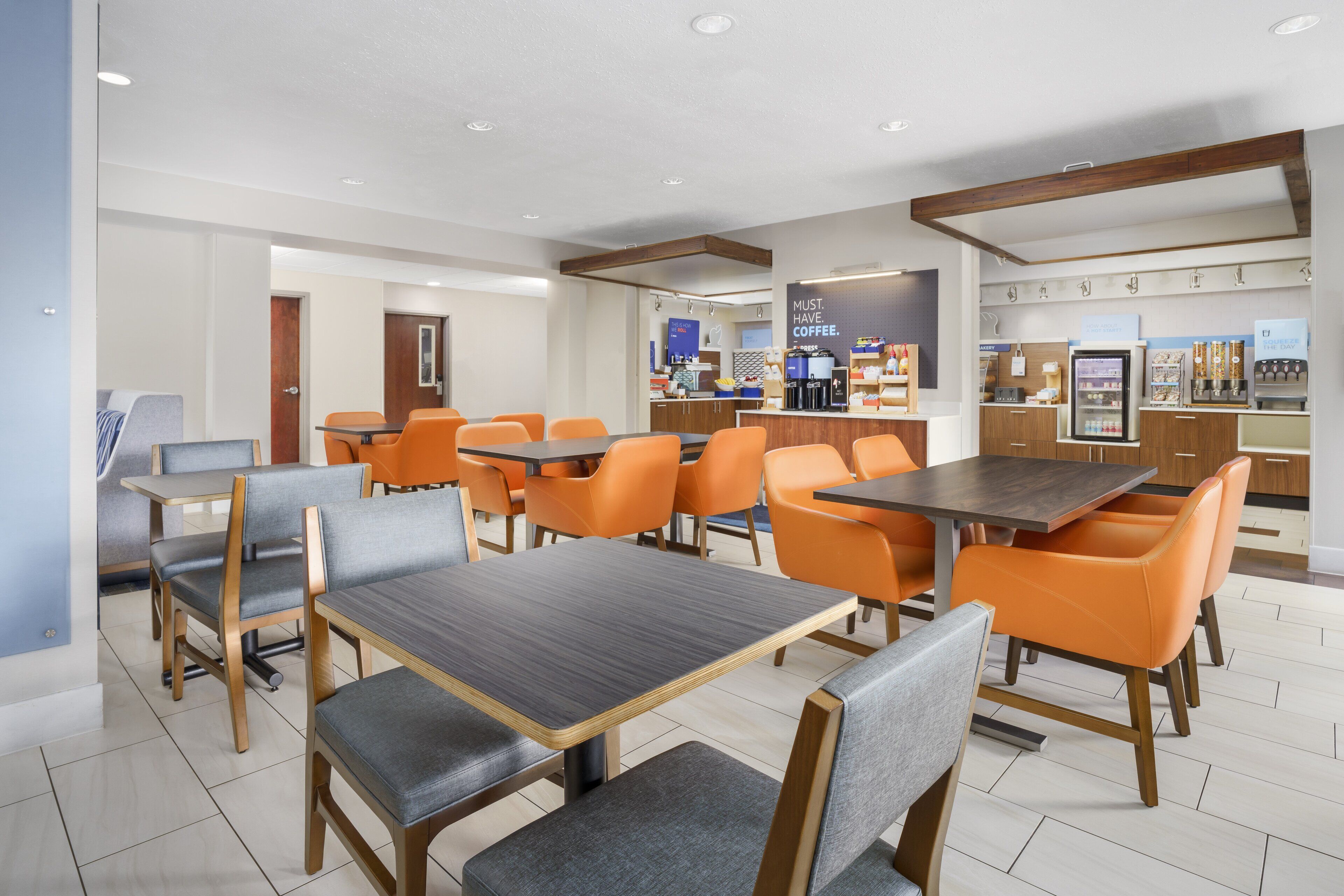 A modern restaurant with multiple tables and chairs, a coffee bar, and a refrigerated display.