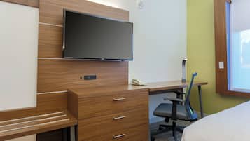 A hotel room with a wooden desk, a flat-screen TV, a telephone, a chair, and a bed.
