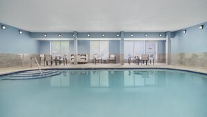 An indoor swimming pool with clear blue water, surrounded by lounge chairs and tables. - Holiday Inn Express Rochester NE- Irondequoit by IHG (Rochester)