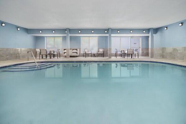 Une piscine intérieure à l’eau d’un bleu limpide, entourée de chaises longues et de tables.