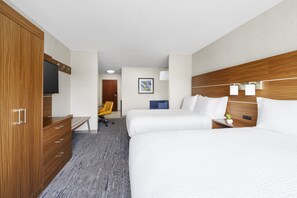 A hotel room with a wooden wardrobe, a desk with a chair, two beds, a television, and a small plant on the nightstand.