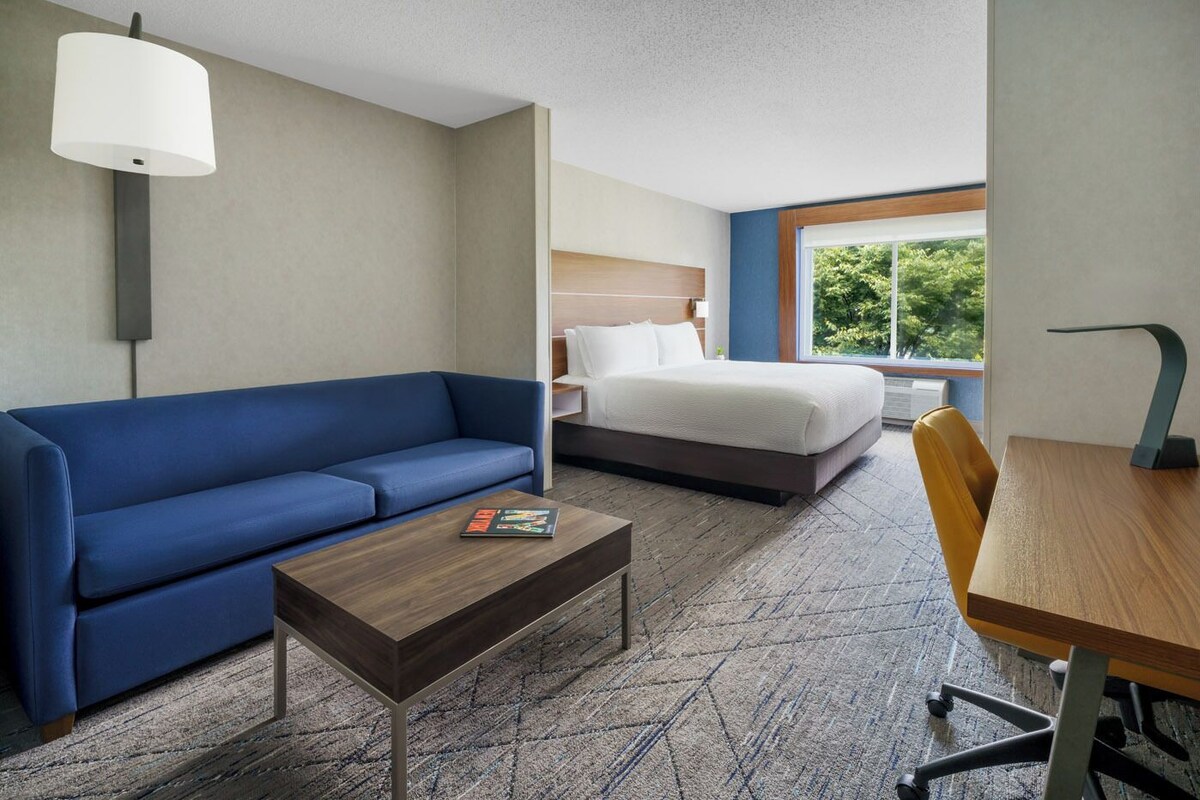 A hotel room with a blue sofa, a wooden coffee table, a bed with white bedding, and a wooden desk with a chair.