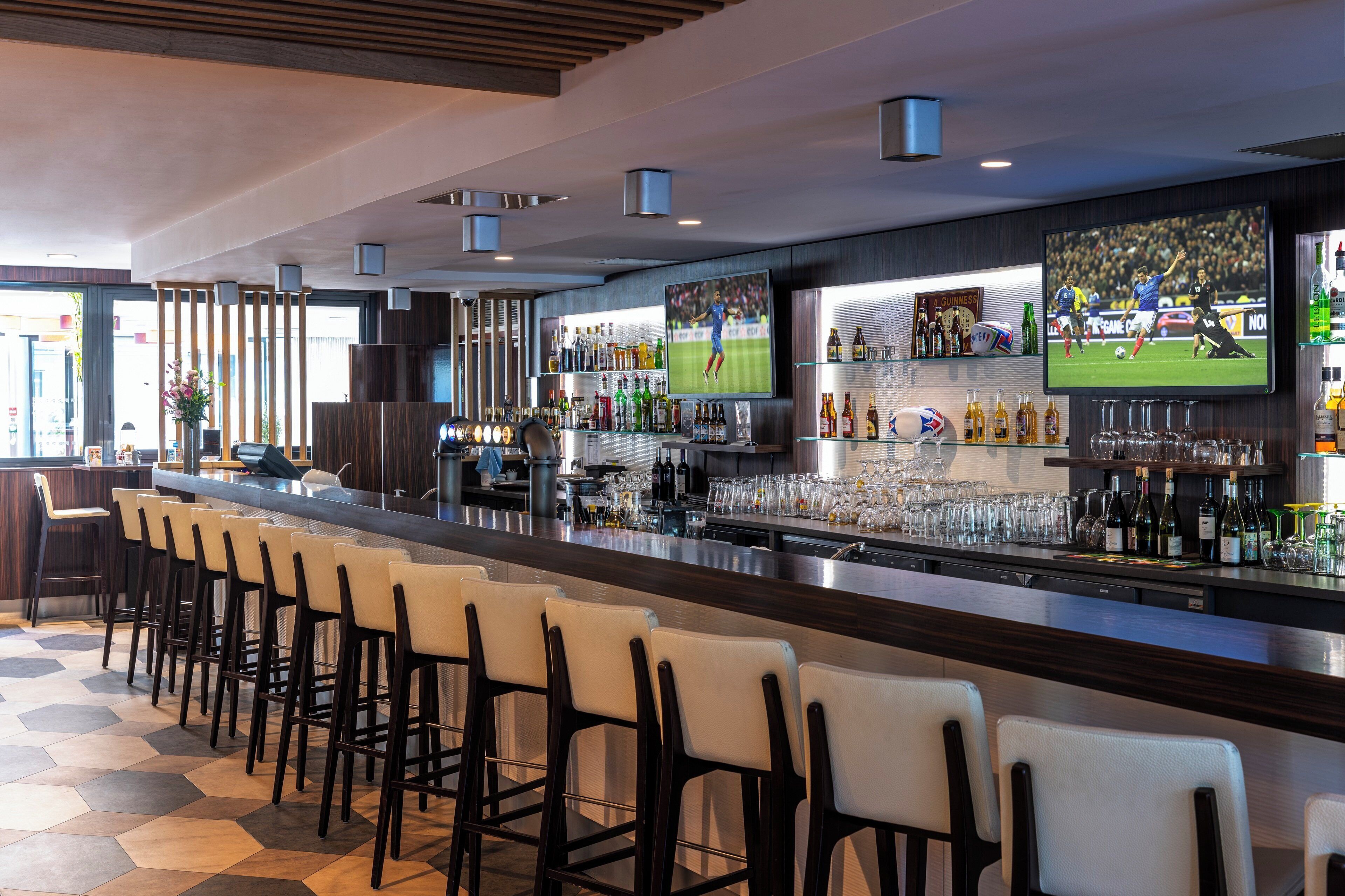 A bar area with a long counter, multiple stools, and a variety of bottles and glasses.