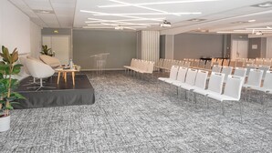 A modern conference room with a carpeted floor, white chairs, a podium, and a sofa. - Holiday Inn Toulouse Airport by IHG (Blagnac)