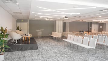 A modern conference room with a carpeted floor, white chairs, a podium, and a sofa.