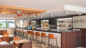 A modern bar area with a wooden ceiling, bar stools, and a counter displaying various bottles and glasses. - Holiday Inn Toulouse Airport by IHG (Blagnac)
