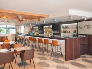 A modern bar area with a wooden ceiling, bar stools, and a counter displaying various bottles and glasses. - Holiday Inn Toulouse Airport by IHG (Blagnac)