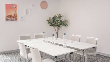 A conference room with a white table, white chairs, a clock, and a poster of a cityscape.
