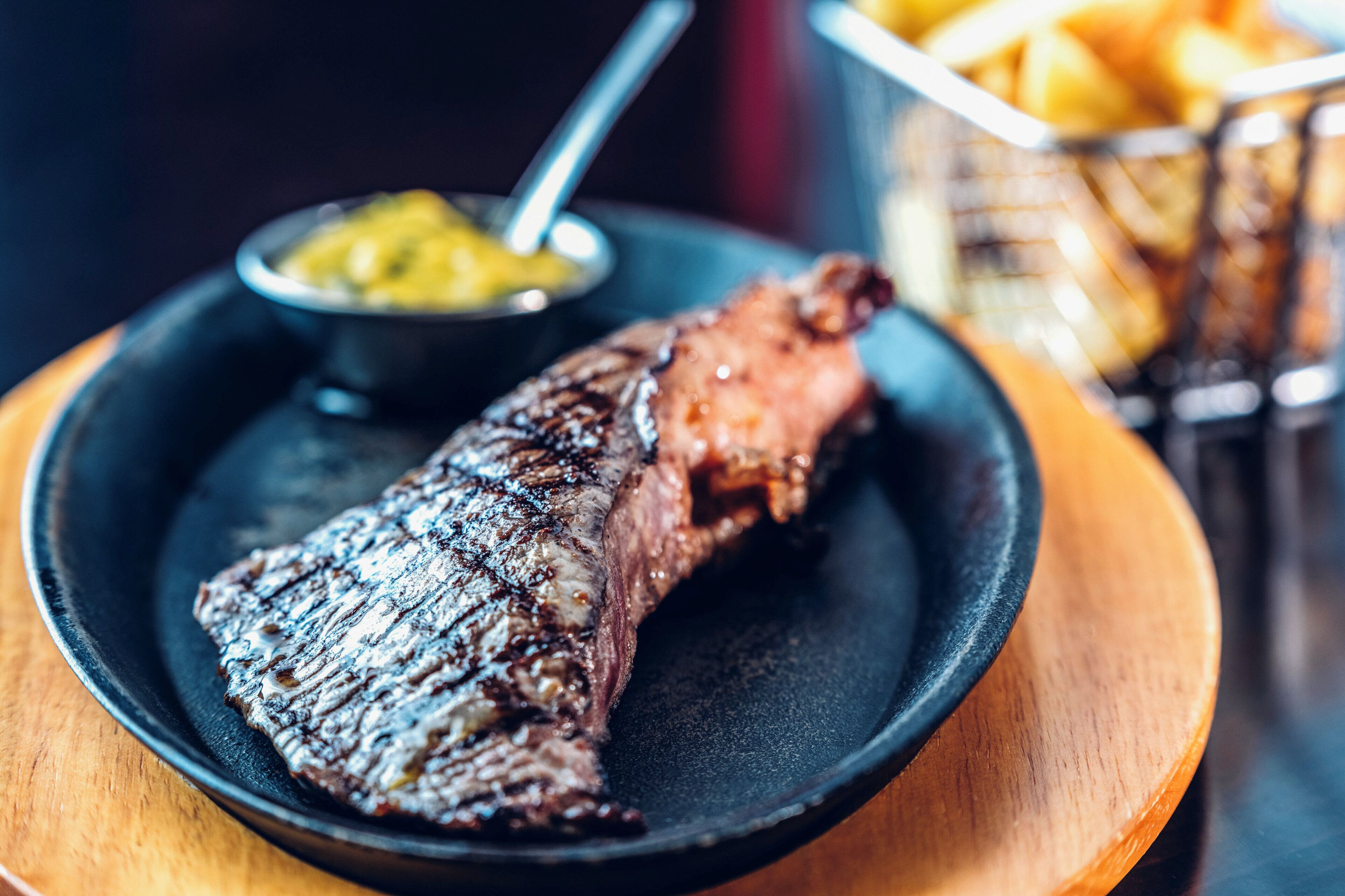 A steak with a side of fries and a small bowl of sauce on a plate.