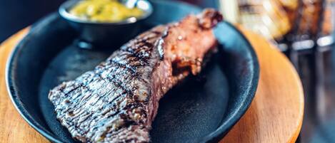 A steak with a side of fries and a small bowl of sauce on a plate.