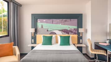 A hotel room with a bed, two bedside tables, a chair, a desk, and a large cityscape artwork on the wall.