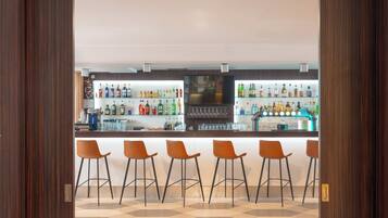 Una zona de bar con mostrador, varios taburetes y estantes llenos de botellas.