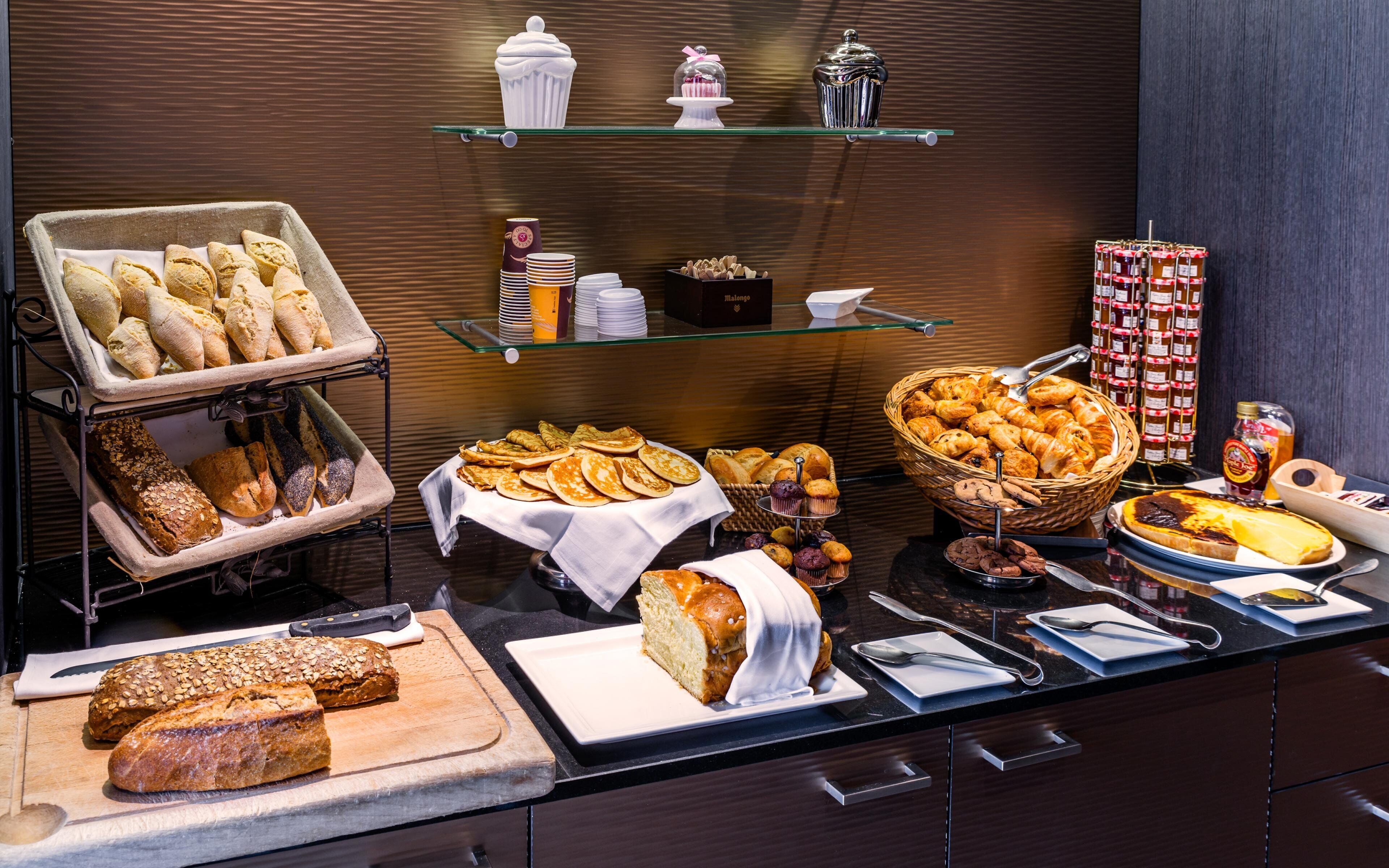 A buffet with various breads, pastries, and a selection of condiments.
